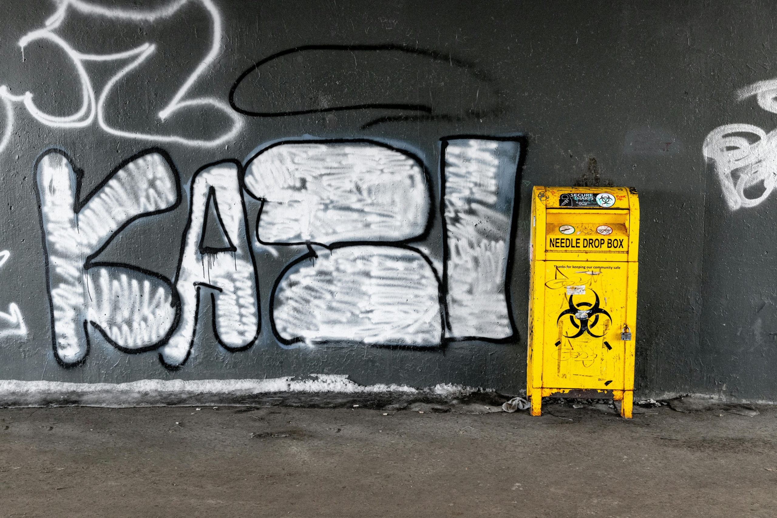 Yellow and Black Garbage Bin Beside Wall With Graffiti